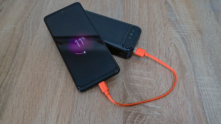 Seorang konten kreator sedang mengisi daya smartphone dan kamera menggunakan power bank portabel di lokasi outdoor.